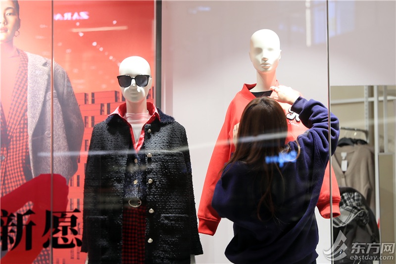 服装店店员为橱窗里的模特穿上新款外套。
