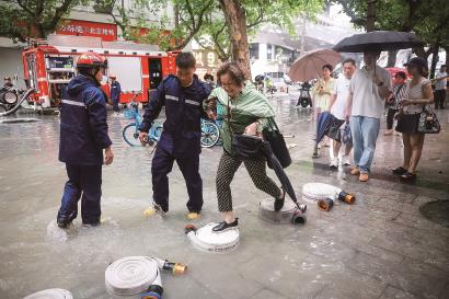 受持续强降雨影响，徐汇区天钥桥路汇联商厦周边积水较为严重，来往于此的市民通行受阻，消防员在天钥桥路用消防水带搭了一座临时“小桥”并搀扶来往行人过积水区。 记者 海沙尔 摄