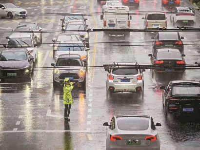 在延安路华山路路口，静安交管支队一大队辅警王戎辰迎风冒雨指挥疏导路口车辆安全通行。 记者 孟雨涵 通讯员 周敏 摄